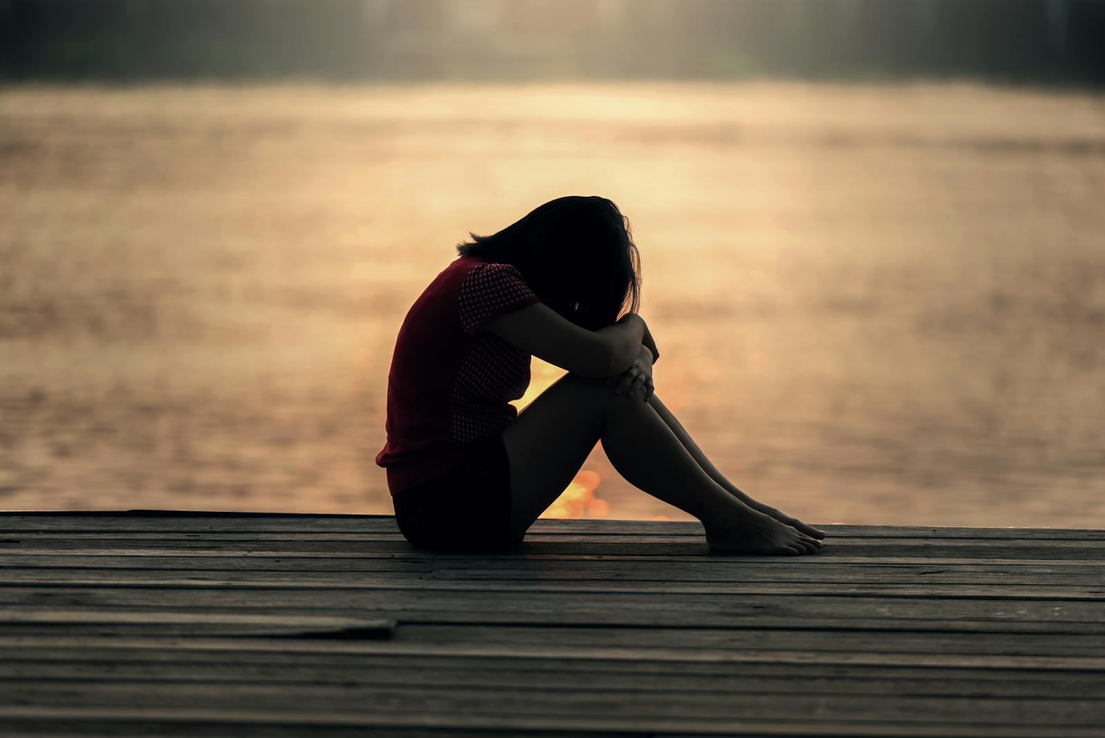 A woman sitting alone on a wooden dock by the lake, showing solitude and reflection. atypical depression