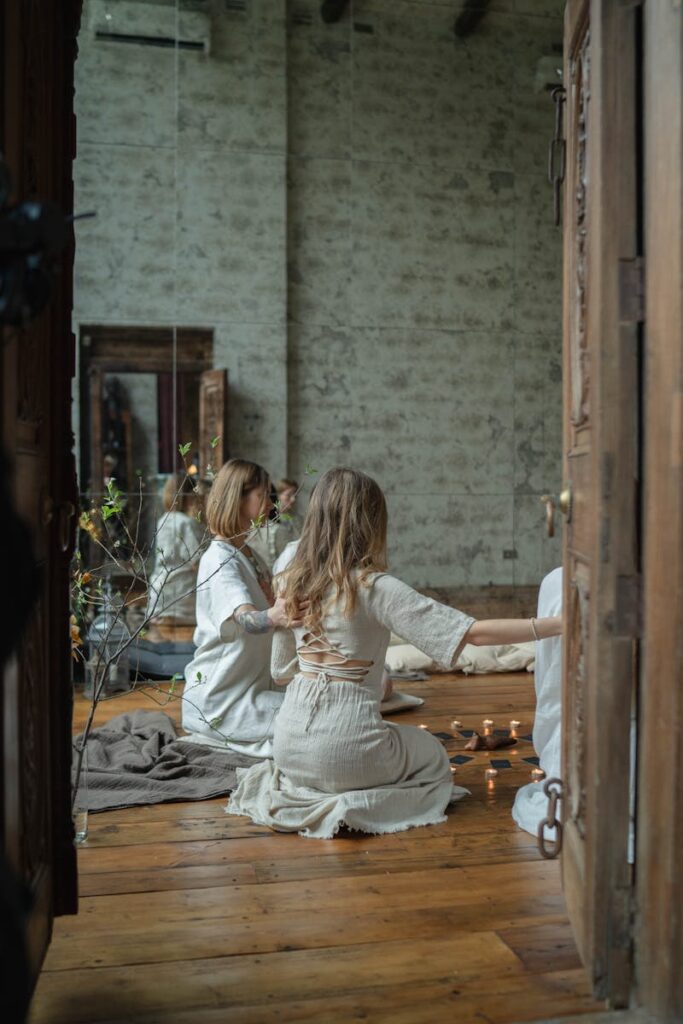 Group of women performing a candlelit spiritual session indoors, surrounded by natural elements.