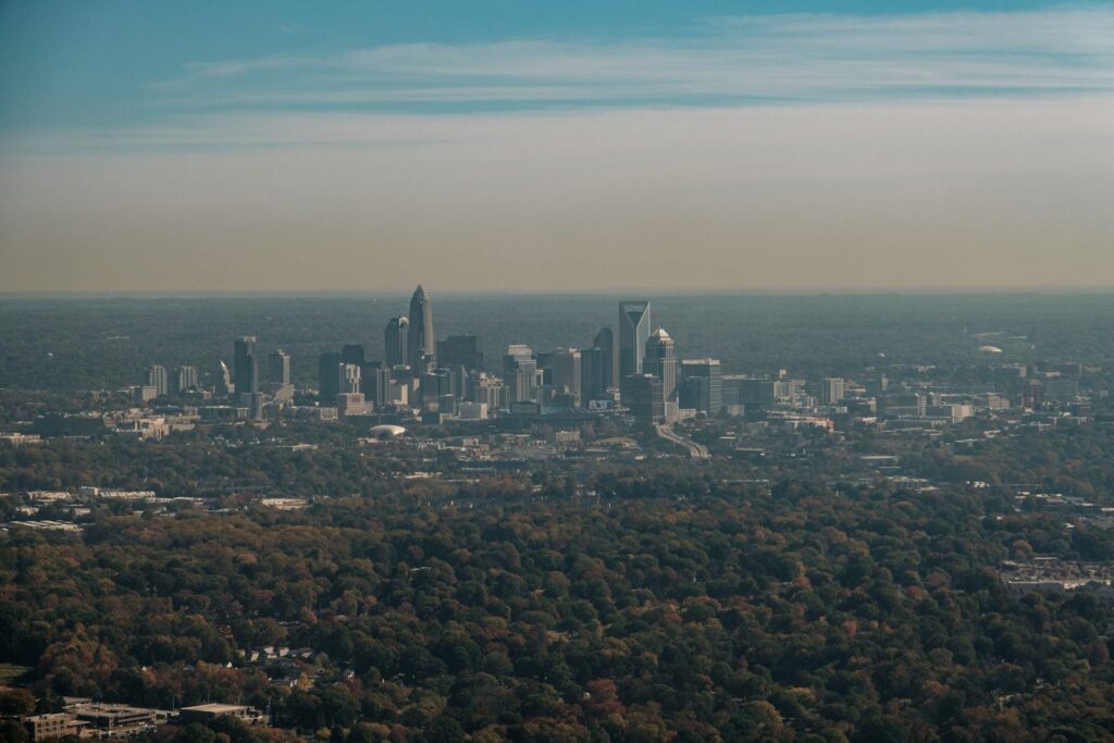 Stunning aerial shot of Charlotte skyline surrounded by fall foliage under a clear sky.