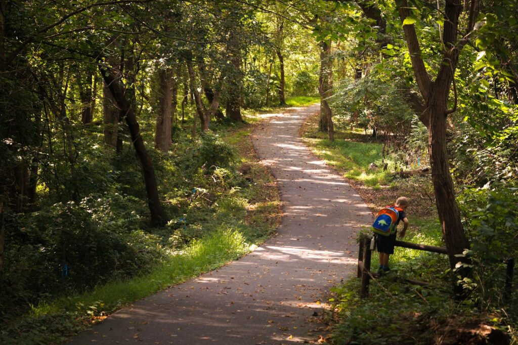 A kid with a colorful backpack explores a wooded trail in Bethesda, Maryland.