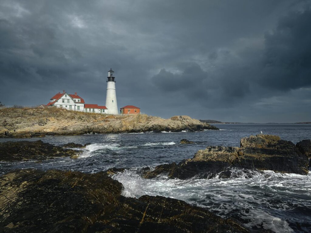 A striking lighthouse on a rocky coast under stormy skies, offering a dramatic marine view.