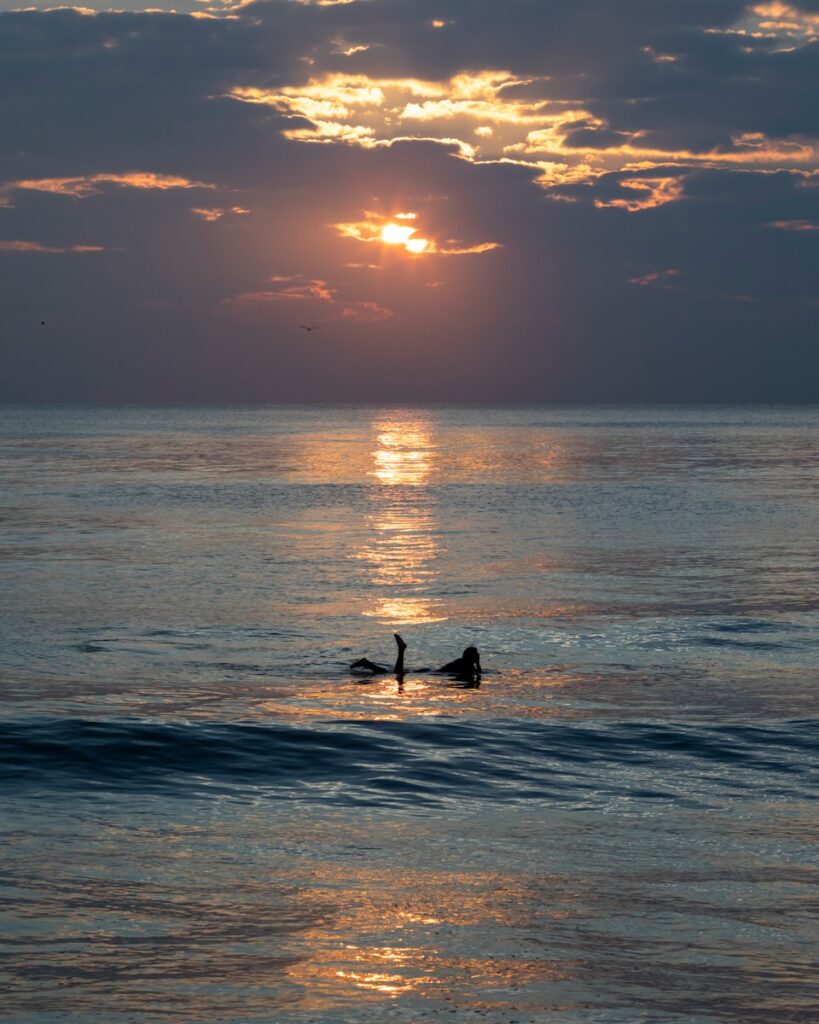 Surfer enjoys the sunrise over the calm ocean.