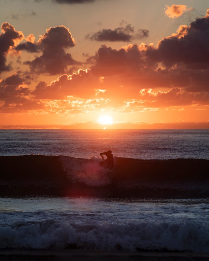 A surfer catches a wave at sunset.