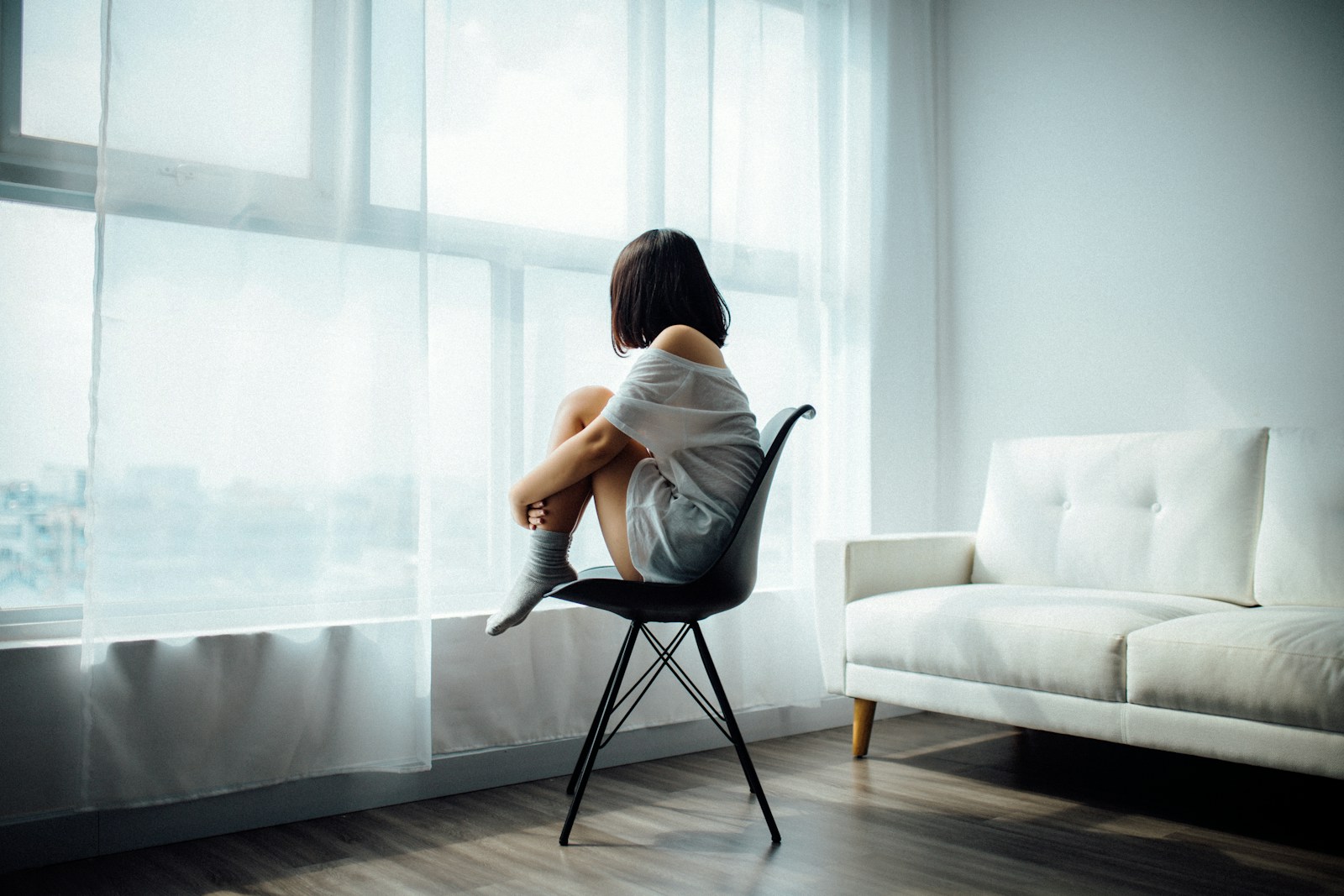 woman sitting on black chair in front of glass-panel window with white curtains Depression