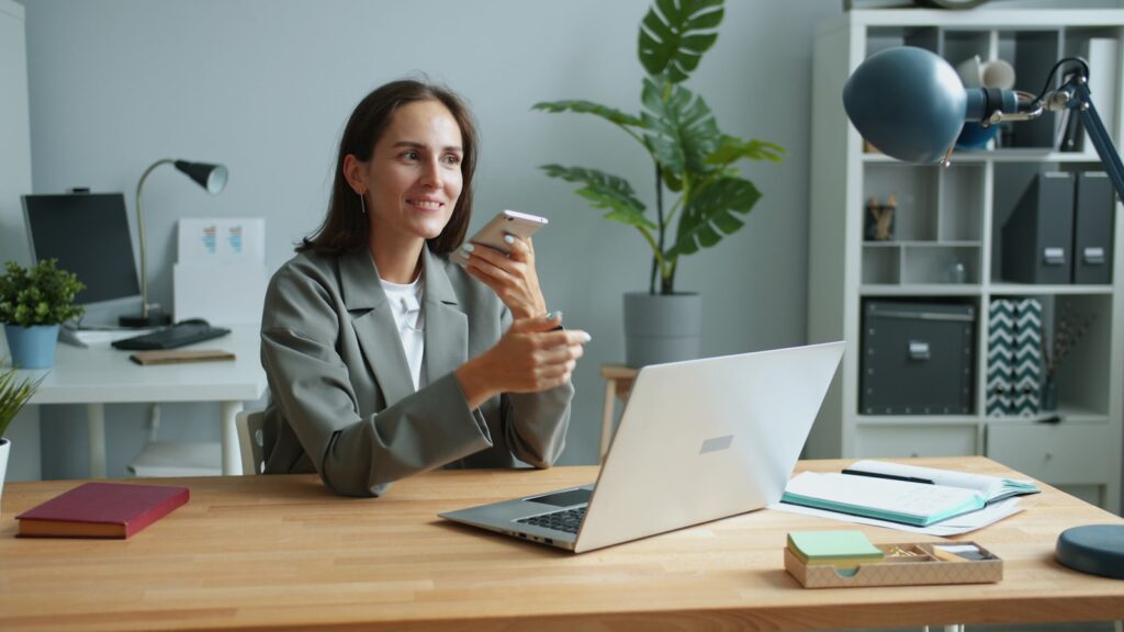Woman talking on phone at desk with laptop.