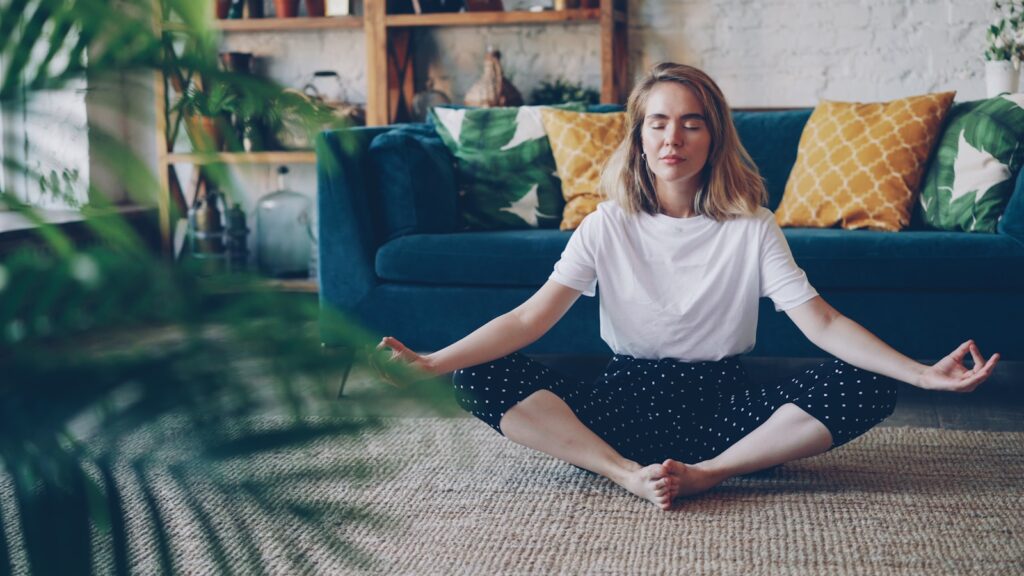 Woman meditating cross-legged on the floor at home.