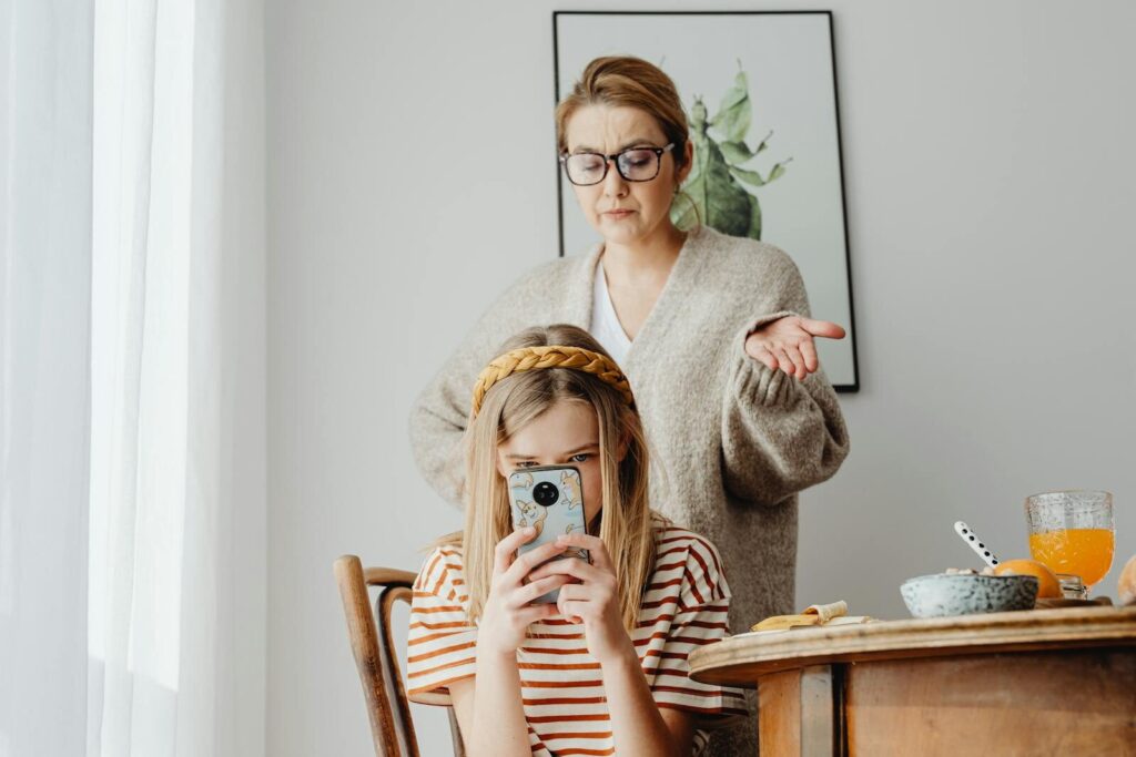 A mother looks upset while her daughter is absorbed in her smartphone.