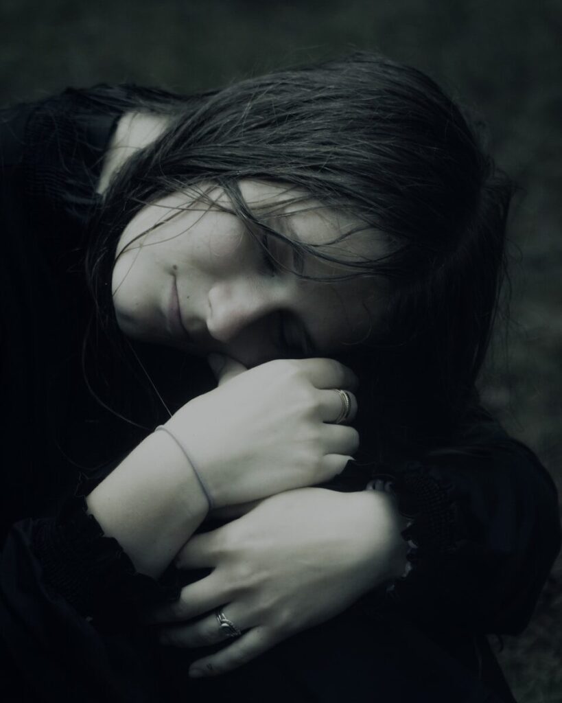 A young woman with dark hair embraces herself.