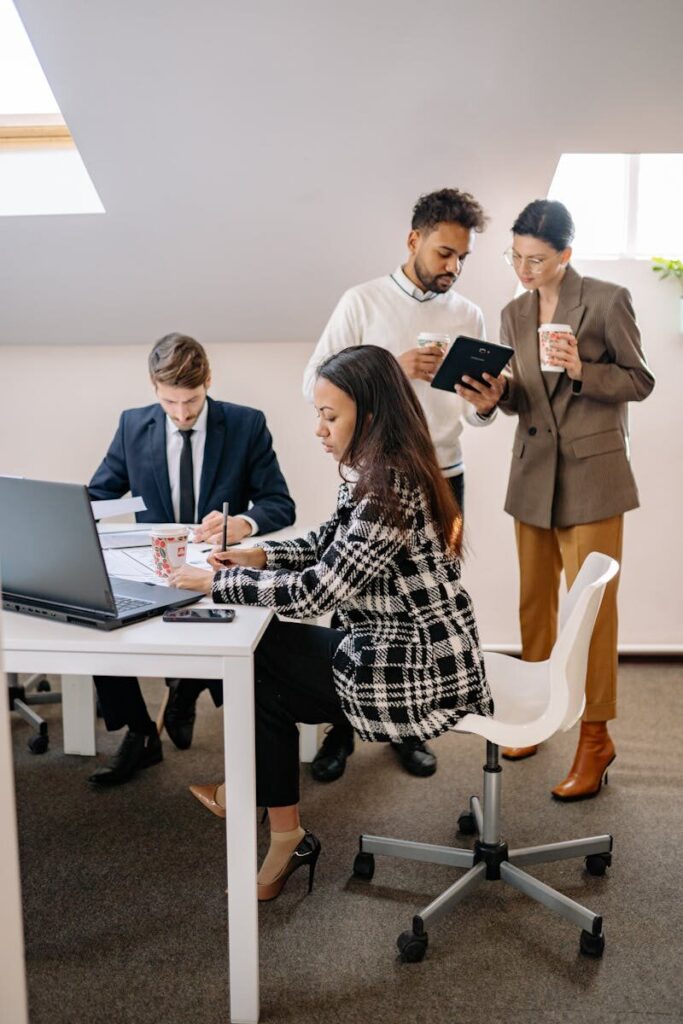 Diverse business team collaborating in an office, working on laptops and discussing projects.
