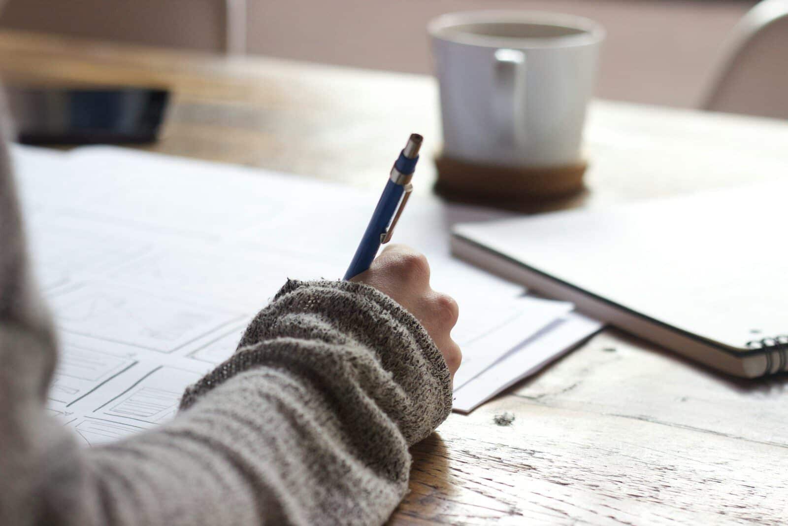 person writing on brown wooden table near white ceramic mug Journal Prompts for Mental Health That Busy CEOs and Professionals Can Actually Use