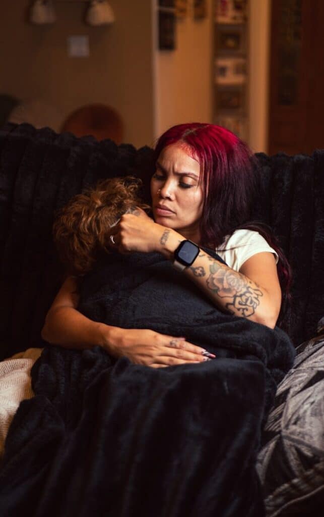 A woman with red hair holding a child wrapped in a black blanket
