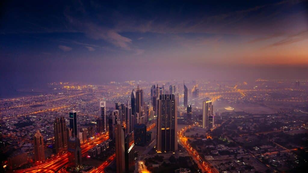 An aerial view of the Dubai skyline at low sun with glowing city lights